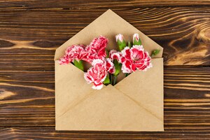 Коричневый конверт с красными цветами гвоздики над деревянным столом