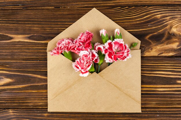 Free photo brown envelope with red carnation flowers over wooden desk