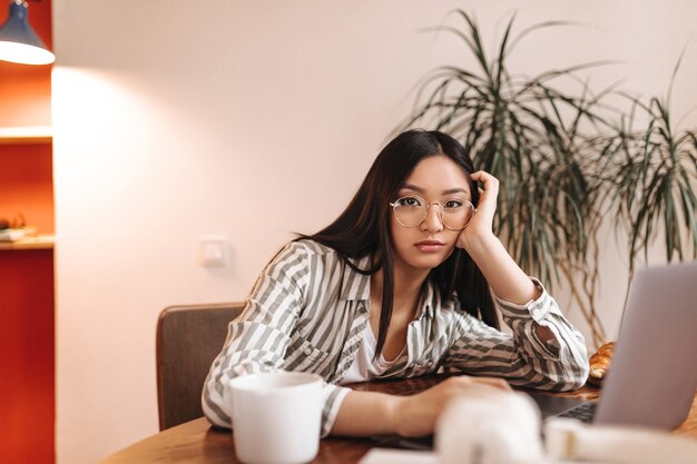 Brown-eyed woman leaned on table and bored looking at front