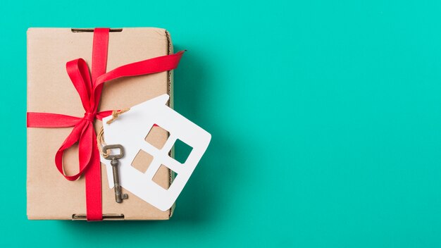 빨간 리본으로 묶어 갈색 선물 상자; 청록색 표면 위의 집 열쇠