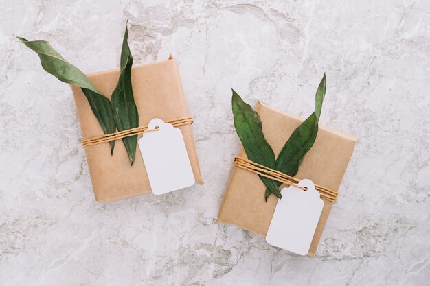 Brown gift boxes with blank tag and leaves on marble backdrop