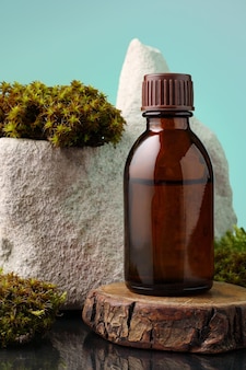 シアンの背景に苔の間に木製のスタンドにエッセンシャルオイルと茶色のガラス瓶。スキンケアや代替医療用のエッセンスリキッド。