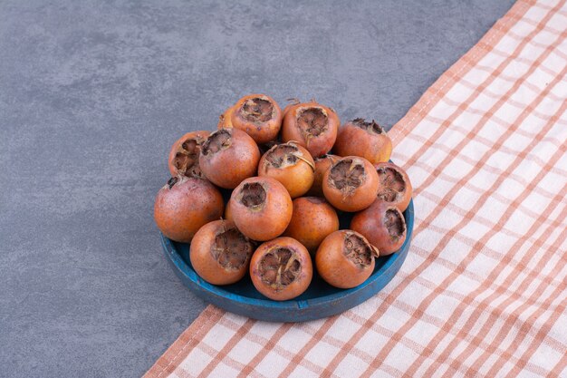 Brown medlars in a blue platter on grey surface