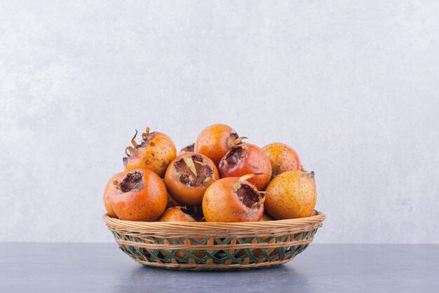 Brown medlars in a wooden platter on blue surface