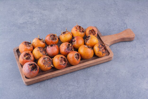 Brown medlars in a wooden platter on blue surface