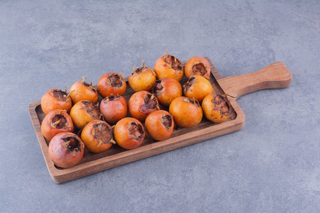 Brown medlars in a wooden platter on blue surface