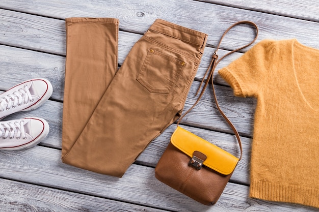 茶色​の​ズボン​と​白い​靴​の​vneckt​シャツ​と​灰色​の​木製​棚​の​バッグ​アパレル服​の​新しい​商品​...