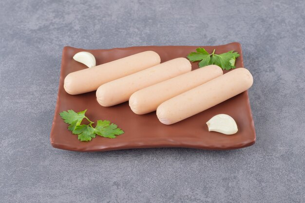 A brown plate of boiled sausages with parsley and garlics 