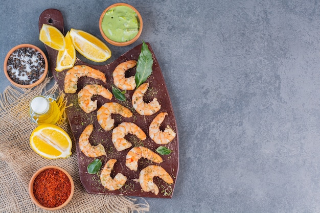 Free photo a brown plate of delicious shrimps with sliced lemon and pepper on a sackcloth