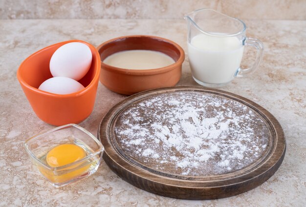 Коричневая тарелка муки и сырых яиц со стаканом молока