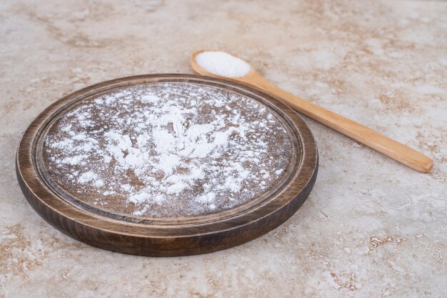 A brown plate of flour and a wooden spoon of sugar