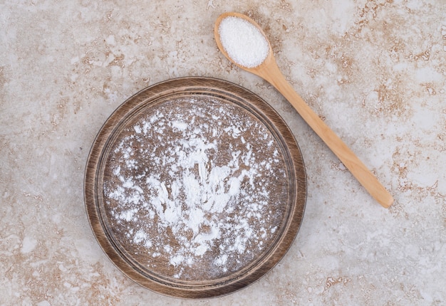 Free photo a brown plate of flour and a wooden spoon of sugar