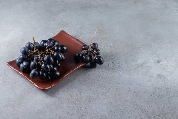 Piatto marrone di uve nere fresche su sfondo di pietra.