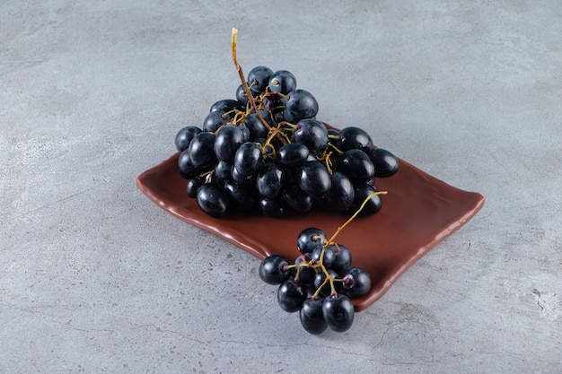 Brown plate of fresh black grapes on stone background. 