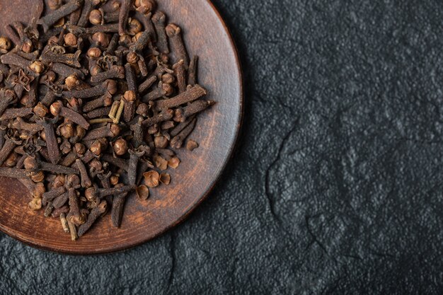 A brown plate full of dried cloves on a dark background . 