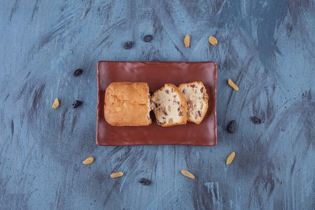 Brown plate of sliced raisin cake on marble surface.