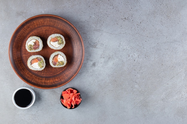 Коричневая тарелка суши-роллов со свежей рыбой на каменном фоне.