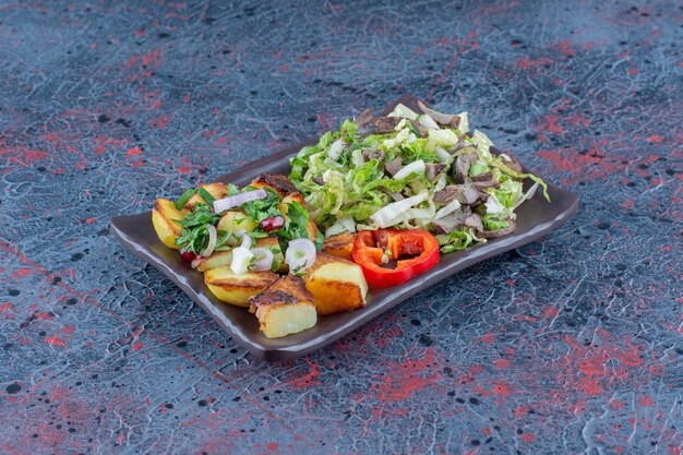 A brown plate of vegetable salad and fried potato . 