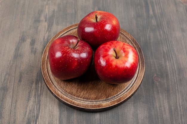 木製のテーブルの上に赤いジューシーなリンゴと茶色のプレート。高品質の写真