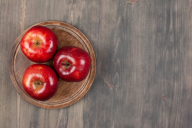 木製のテーブルの上に赤いジューシーなリンゴと茶色のプレート。高品質の写真