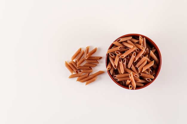 brown raw pasta in bowl top view on white surface