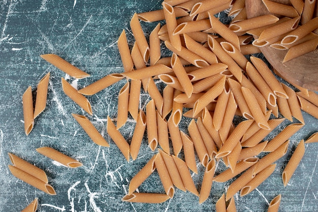 Free photo brown raw penne pasta on blue background. high quality photo
