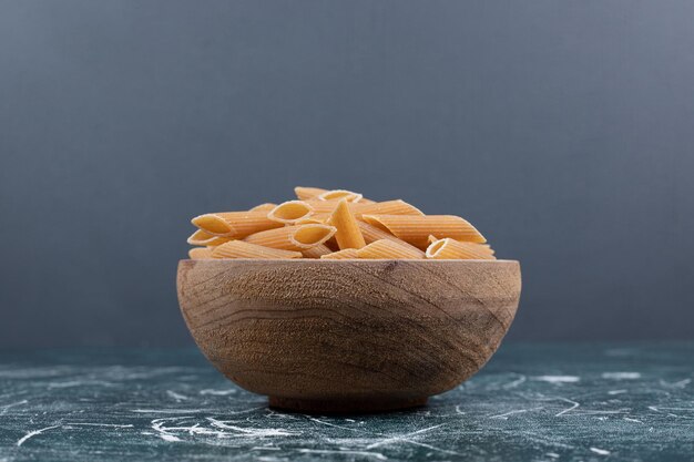 Brown raw penne pasta in wooden bowl. 