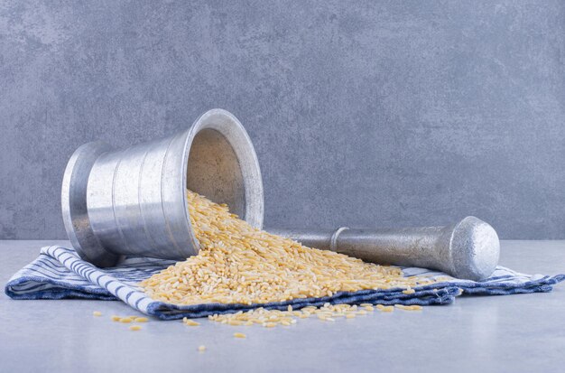 Brown rice pouring out of herb masher on a towel on marble surface