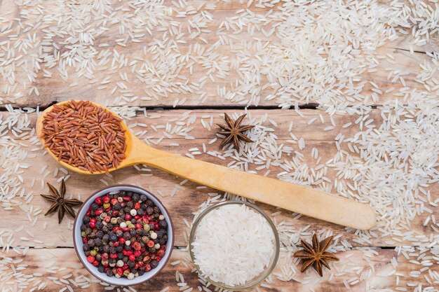 Коричневый рис в деревянной ложке с перцем и анисом на деревенском деревянном фоне