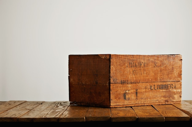 Brown rustic wooden wine box with barely legible black letters on a wooden table against white wall background