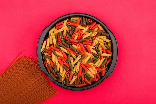 brown spaghetti and different color pasta in black bowl on pink surface