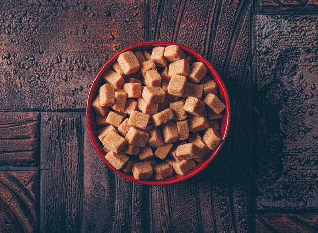 Brown sugar cubes in a bowl on a dark wooden table. flat lay.