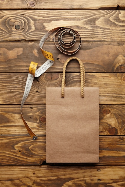 Коричневая сумка на вынос из этой переработанной крафт-бумаги на деревенском деревянном столе рядом с развернутым винтажным портняжным счетчиком