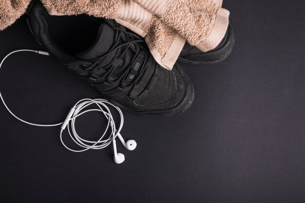 Brown towel on pair of shoes with white ear phone on black background