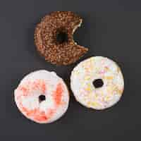 Free photo brown and white bitten doughnuts with sprinkles on black background