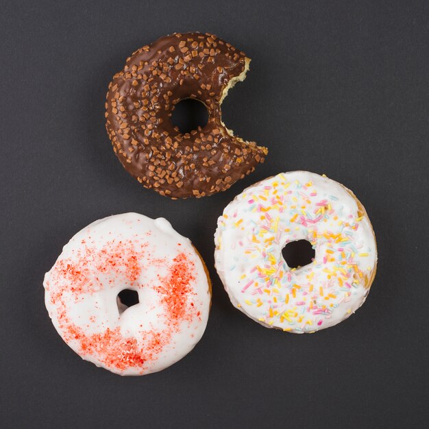 Brown and white bitten doughnuts with sprinkles on black background