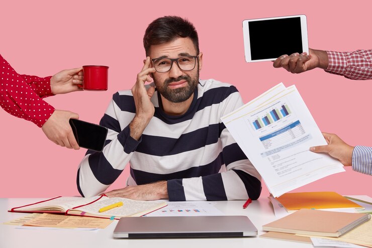 Brunet man sitting at desk surrounded with gadgets and papers