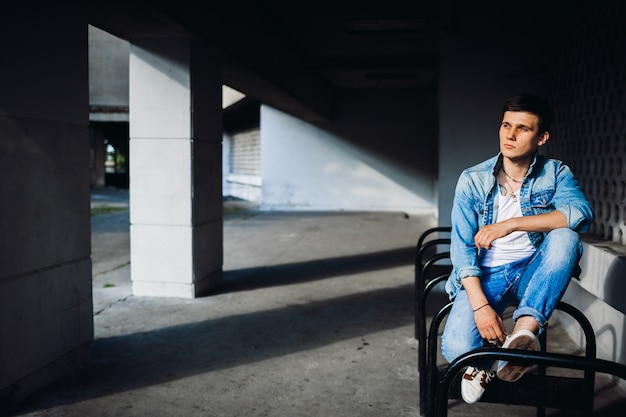 Brunette boy in jeans jacket poses outside 