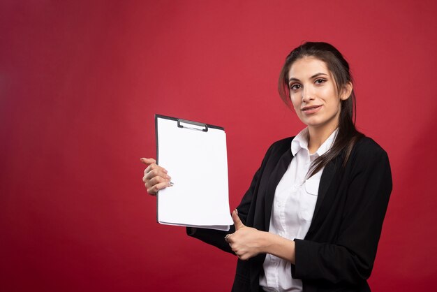 Brunette businesswoman holding clipboard and giving thumbs up. 
