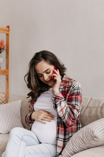 Brunette cheerful pregnant woman in plaid shirt and white tee talks on phone