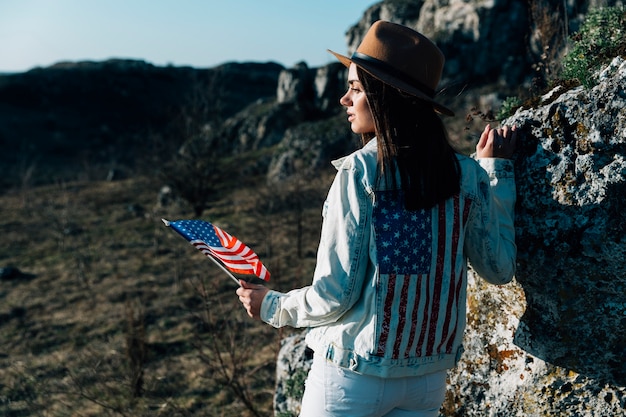 Brunette in denim jacket holding American flag on nature