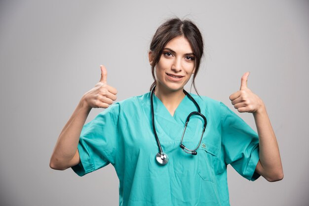 Brunette doctor with stethoscope posing on gray