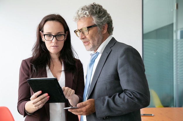 Brunette female assistant showing data to boss and holding tablet