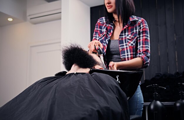 サロンでひげを生やした男性のクライアントの髪を洗うブルネットの女性美容師。