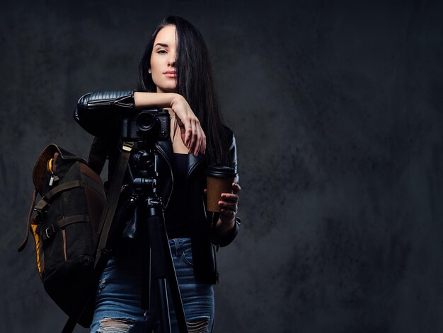 Brunette female photographer holds professional camera on a tripod and traveler backpack.