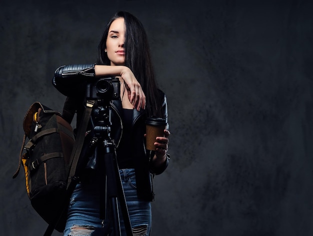 Brunette female photographer holds professional camera on a tripod and traveler backpack.