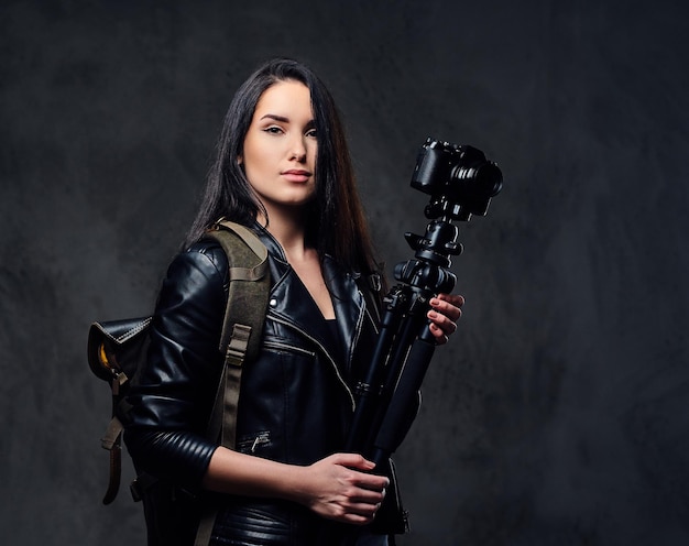 Brunette female photographer holds professional camera on a tripod and traveler backpack.
