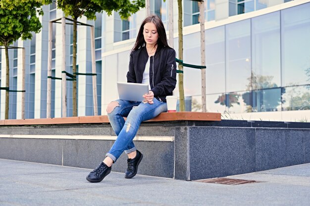 Brunette female student using tablet PC on a city street.