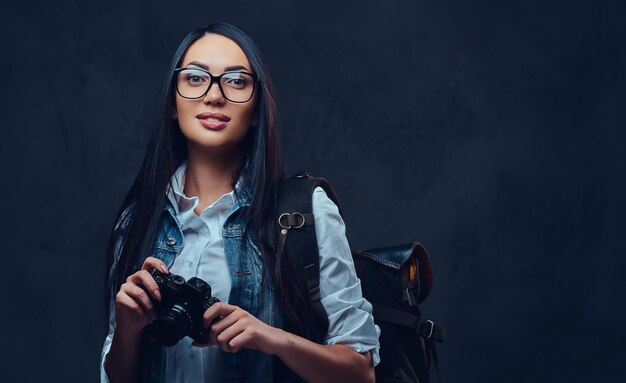 A brunette female traveler with backpack holds compact photo camera.