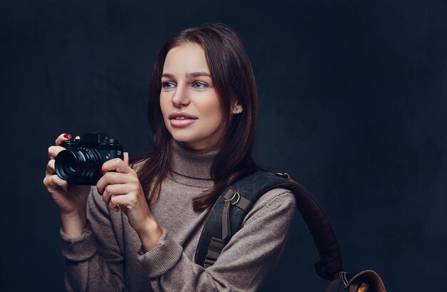 A brunette female traveler with backpack holds compact photo camera.